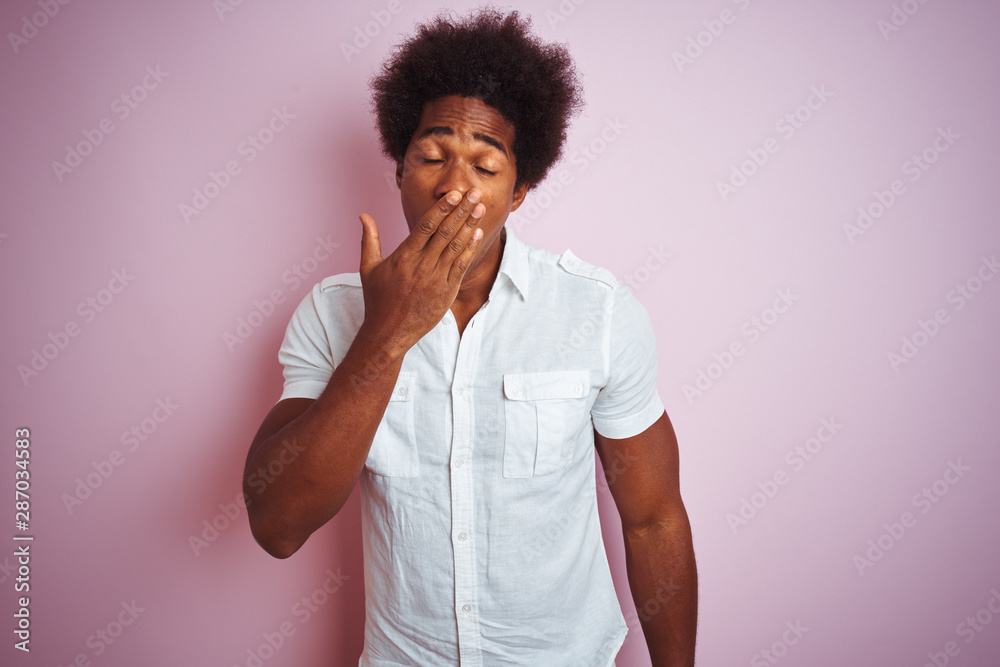 Young american man with afro hair wearing white shirt standing over isolated pink background bored yawning tired covering mouth with hand. Restless and sleepiness.
