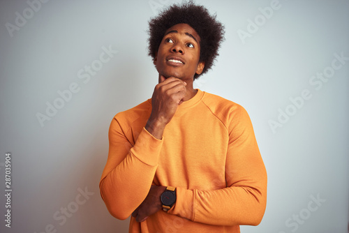 Young american man with afro hair wearing orange sweater over isolated white background with hand on chin thinking about question, pensive expression. Smiling with thoughtful face. Doubt concept. © Krakenimages.com