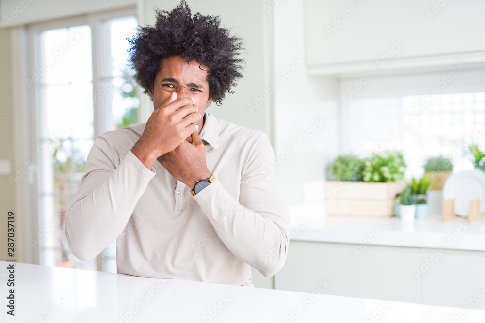 African American man at home smelling something stinky and disgusting, intolerable smell, holding breath with fingers on nose. Bad smells concept. African American man at home smelling something stinky and disgusting, intolerable smell, holding breath with fingers on nose. Bad smells concept.