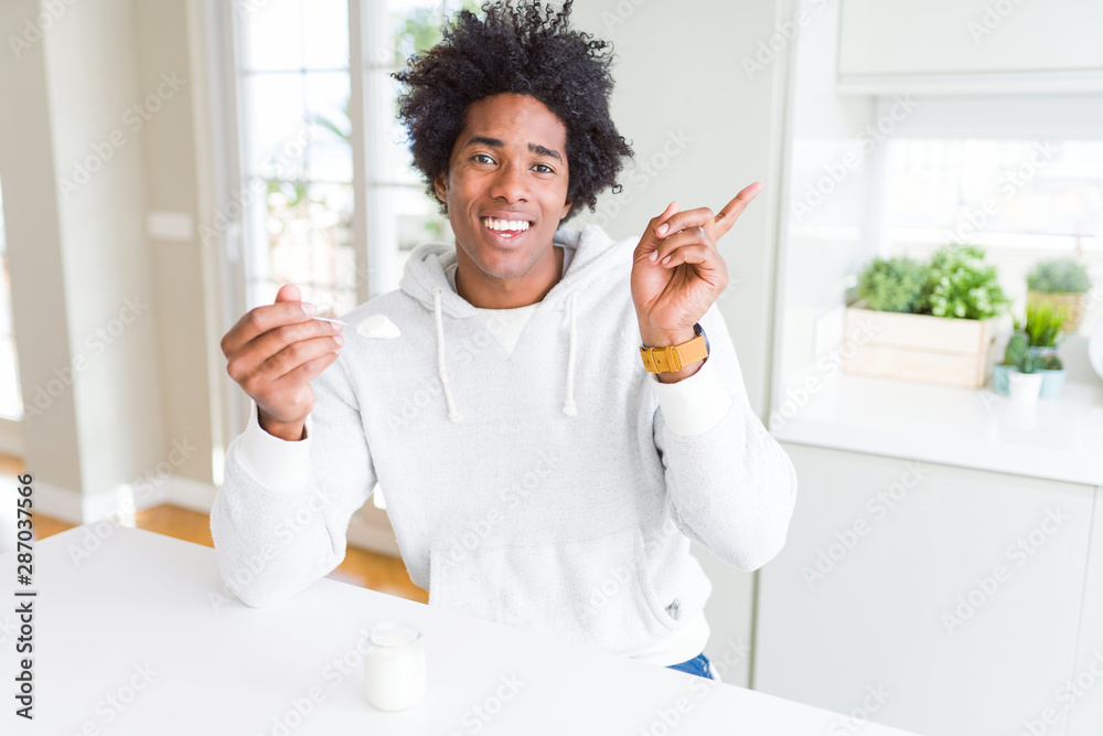 African American man eating healthy yogurt for breakfast very happy pointing with hand and finger to the side
