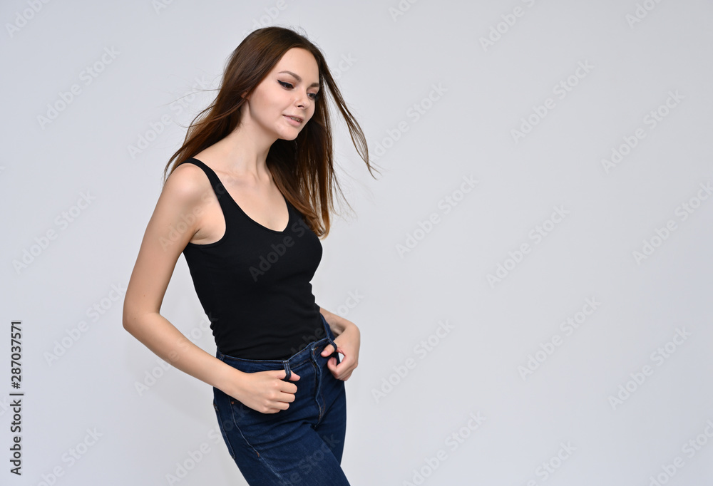 Portrait of a cute brunette girl, a young woman with beautiful curly hair in a black T-shirt on a white background. Smiling, talking with emotions, showing hands to the sides. Portrait of a cute brunette girl, a young woman with beautiful curly hair in a black T-shirt on a white background. Smiling, talking with emotions, showing hands to the sides.