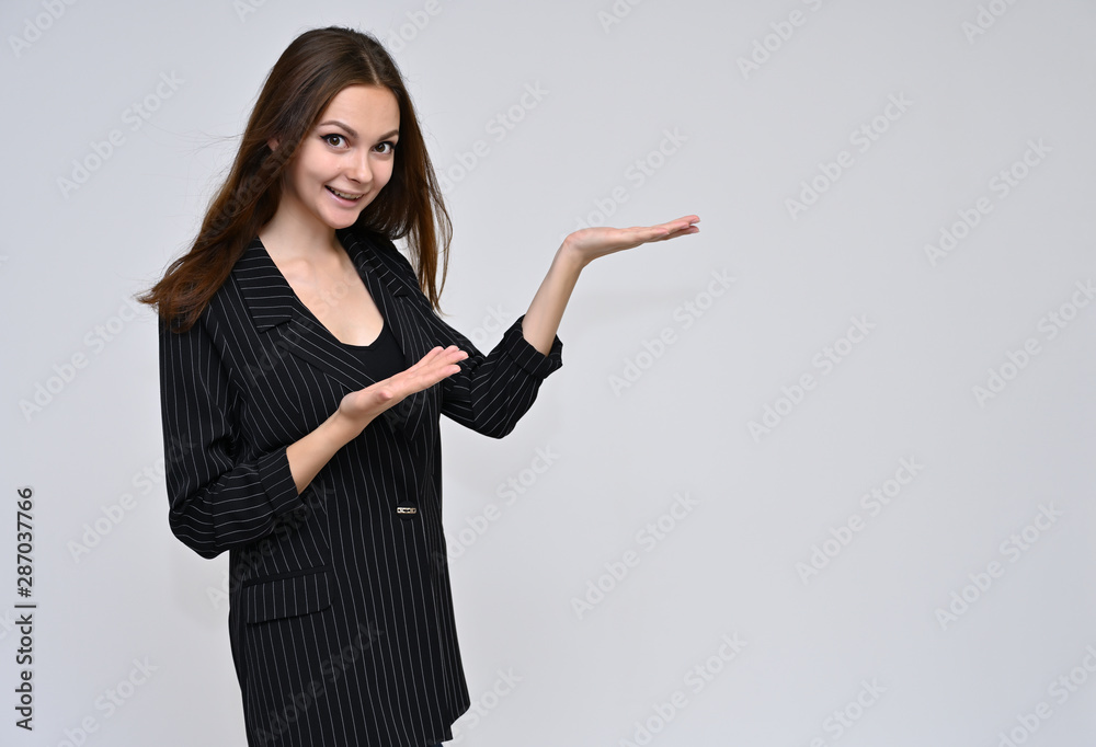 Portrait of a cute brunette girl, a young woman with beautiful curly hair in a black jacket on a white background. Smiling, talking with emotions, showing hands to the sides. Portrait of a cute brunette girl, a young woman with beautiful curly hair in a black jacket on a white background. Smiling, talking with emotions, showing hands to the sides.