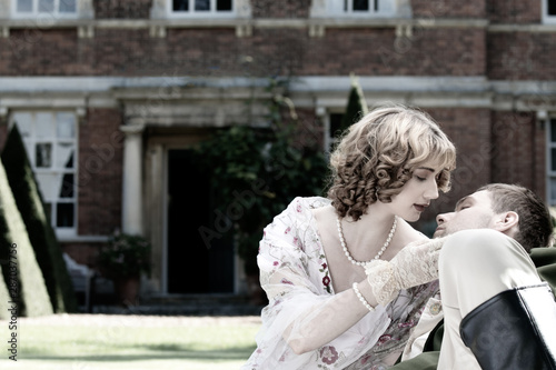 Young couple dressed in vintage costume relaxing and kissing on lawn of stately home © Tony Marturano