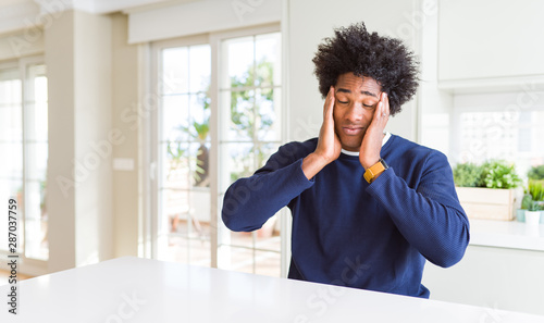 Young african american man wearing casual sweater sitting at home with hand on headache because stress. Suffering migraine.