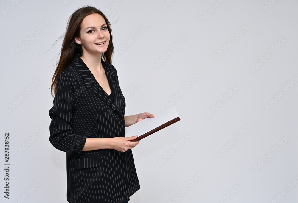 Portrait of a cute brunette girl, a young woman with beautiful curly hair in a black jacket with a folder in her hands on a white background. Smiling, talking with emotions, showing hands. Portrait of a cute brunette girl, a young woman with beautiful curly hair in a black jacket with a folder in her hands on a white background. Smiling, talking with emotions, showing hands.