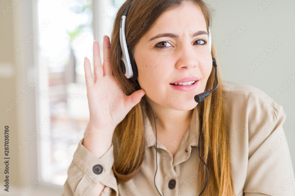 Beautiful young operator woman wearing headset at the office smiling with hand over ear listening an hearing to rumor or gossip. Deafness concept. Beautiful young operator woman wearing headset at the office smiling with hand over ear listening an hearing to rumor or gossip. Deafness concept.