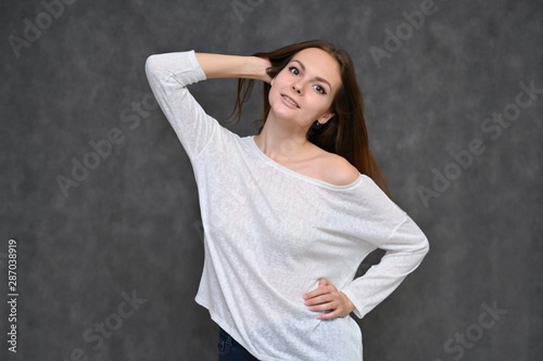 Portrait of a cute brunette girl, a young woman with beautiful curly hair in a white sweater on a gray background. Smiling, talking with emotions, showing hands to the sides. photo
