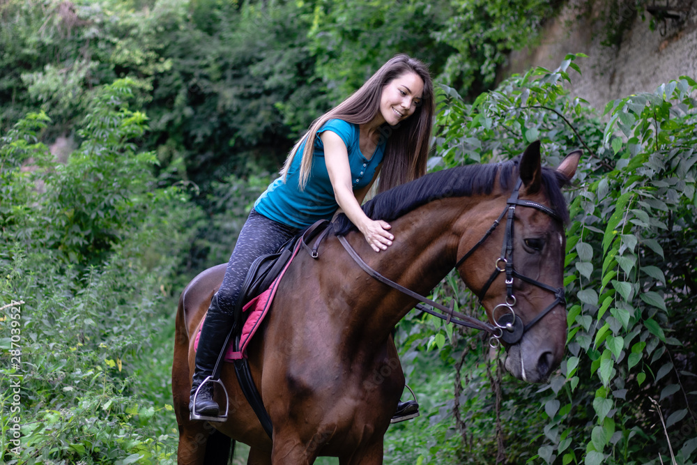Young beautiful brunette girl riding on a horse in the park.