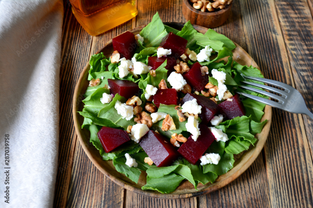 Warm autumn beetroot salad with soft cheese, walnuts and spinach in a plate on a wooden background