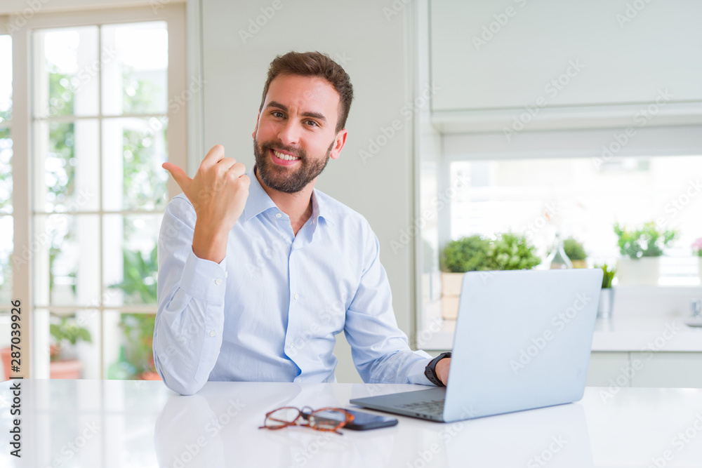Handsome business man working using computer laptop pointing and showing with thumb up to the side with happy face smiling