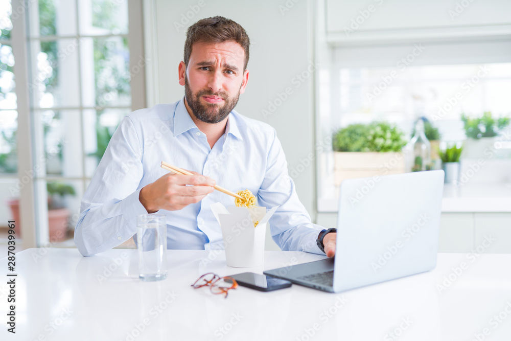 Business man eating take away asian noodles food while working using computer laptop and smiling