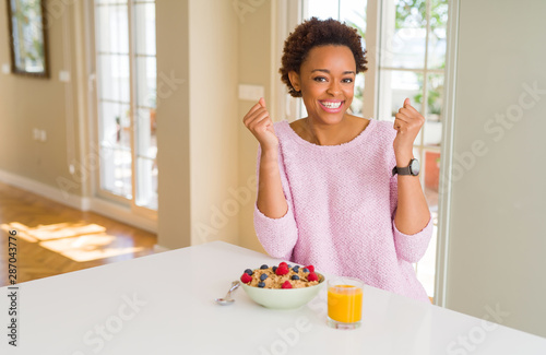 Young african american woman having healthy breakfast in the morning at home celebrating surprised and amazed for success with arms raised and open eyes. Winner concept.
