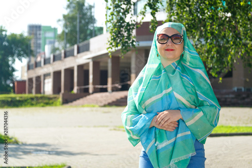A young Muslim woman in a light scarf and glasses in the street.