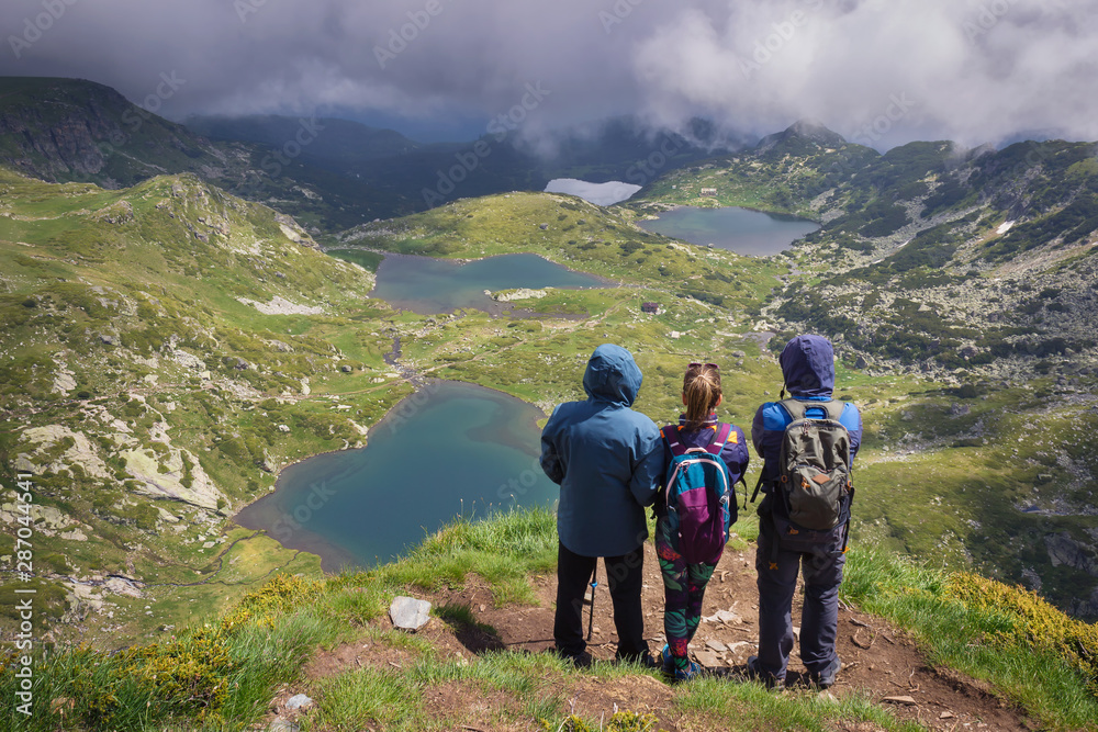 Father, daughter and son standing at the edge of Lake peak, famous vantage point of seven Rila lakes, and looking from above at amazing glacial lakes through the thick fog