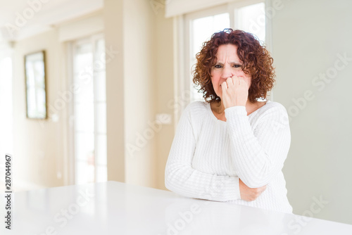 Beautiful senior woman wearing white sweater at home looking stressed and nervous with hands on mouth biting nails. Anxiety problem. © Krakenimages.com