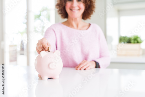 Close up of senior woman putting a coin inside piggy bank as savings smiling confident