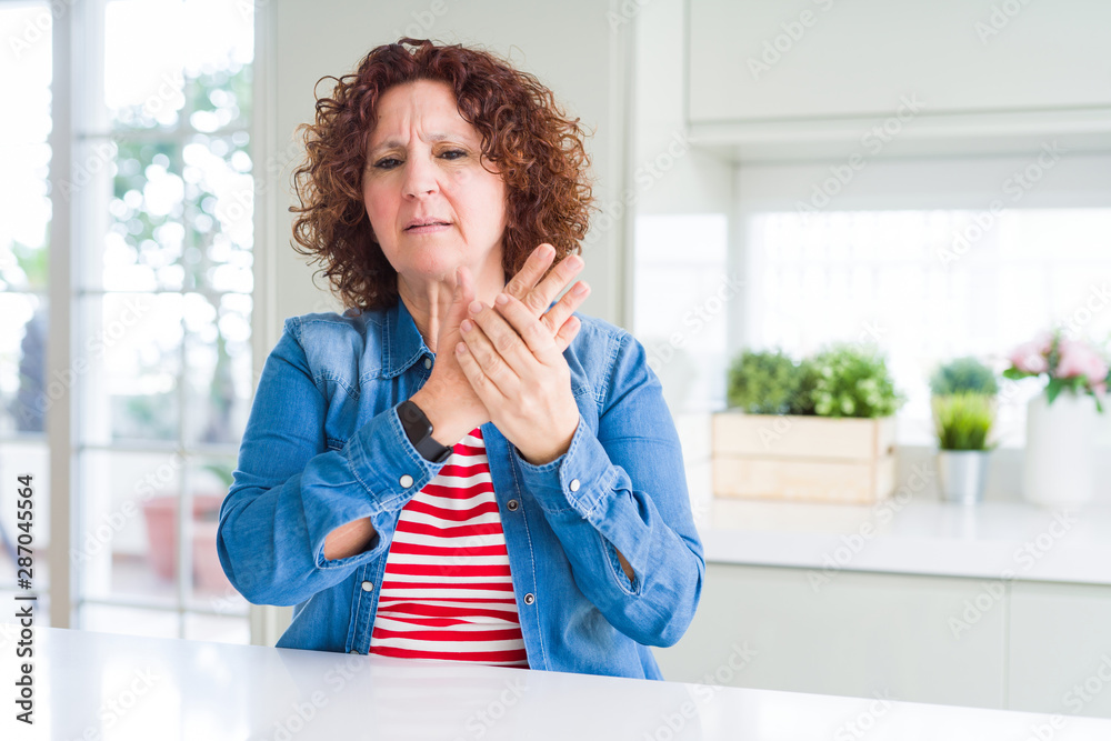 Middle age senior woman with curly hair wearing denim jacket at home Suffering pain on hands and fingers, arthritis inflammation Middle age senior woman with curly hair wearing denim jacket at home Suffering pain on hands and fingers, arthritis inflammation