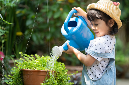 Asian little child girl pouring water on the trees. kid helps to care for the plants with a watering can in the garden.