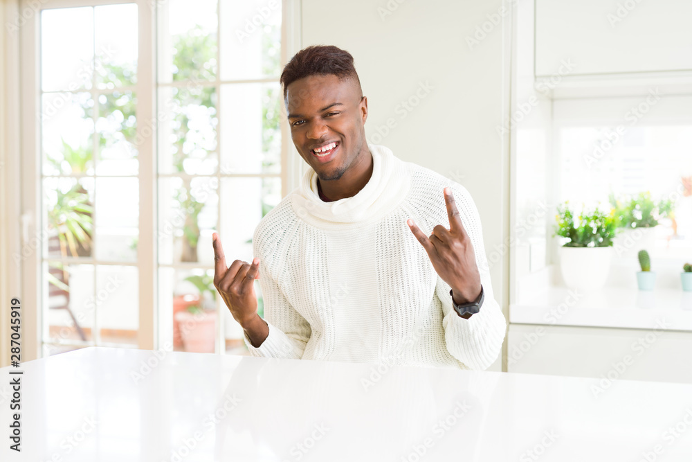 Handsome african american man on white table shouting with crazy expression doing rock symbol with hands up. Music star. Heavy concept. Handsome african american man on white table shouting with crazy expression doing rock symbol with hands up. Music star. Heavy concept.
