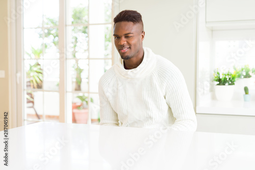 Handsome african american man on white table winking looking at the camera with sexy expression, cheerful and happy face.