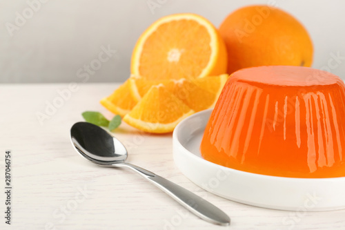 Plate with tasty orange jelly served on white wooden table, space for text