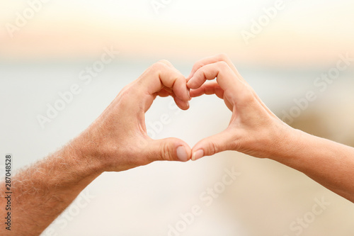 Happy couple making heart with their hands against blurred landscape © New Africa