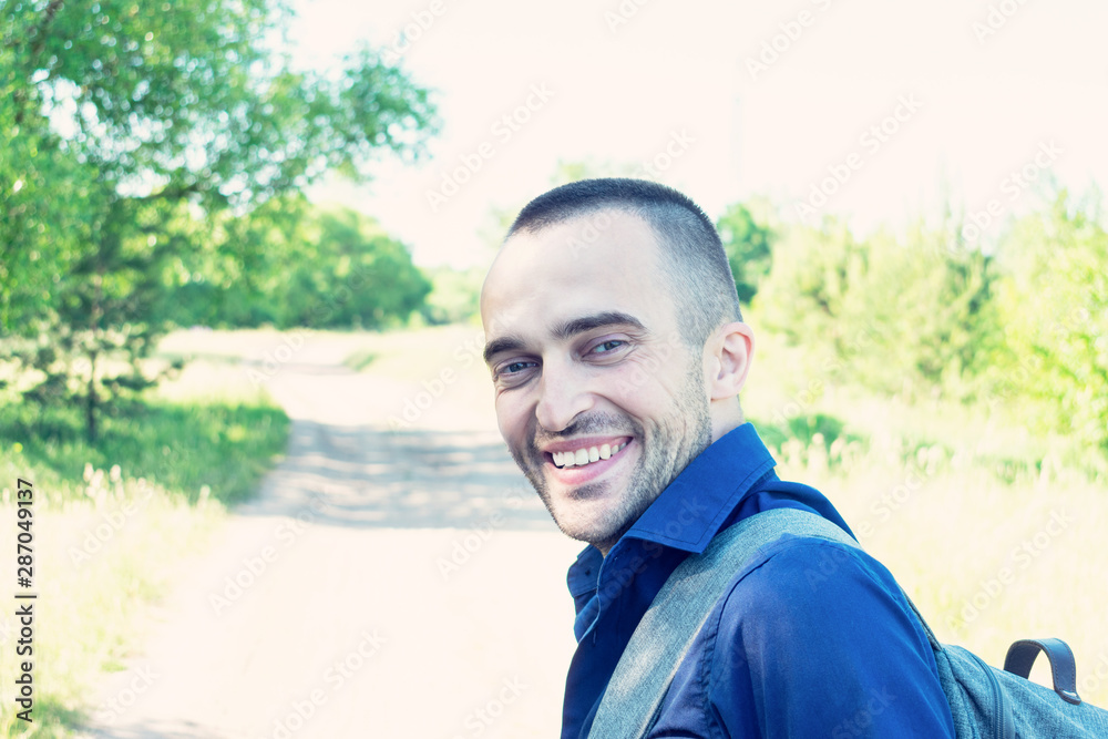 A traveler goes on the road, man with a backpack looks back and smiles at the camera, portrait, toned A traveler goes on the road, man with a backpack looks back and smiles at the camera, portrait, toned