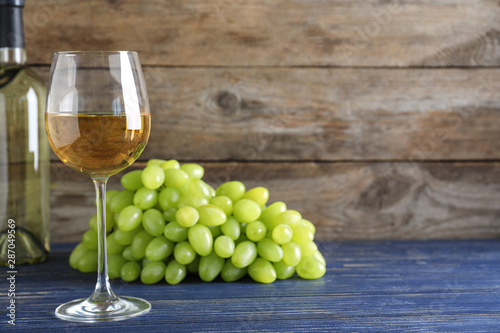 Fresh ripe juicy grapes and wine on blue table against wooden background. Space for text