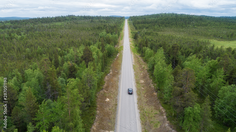 Car on straight road between forest. Cloudy sky. Aerial view.