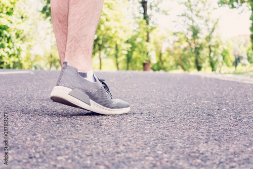 Sportsman walking on the road in the Park in the summer, the man's feet in sneakers, closeup, cropped image, toned. The concept of Hiking
