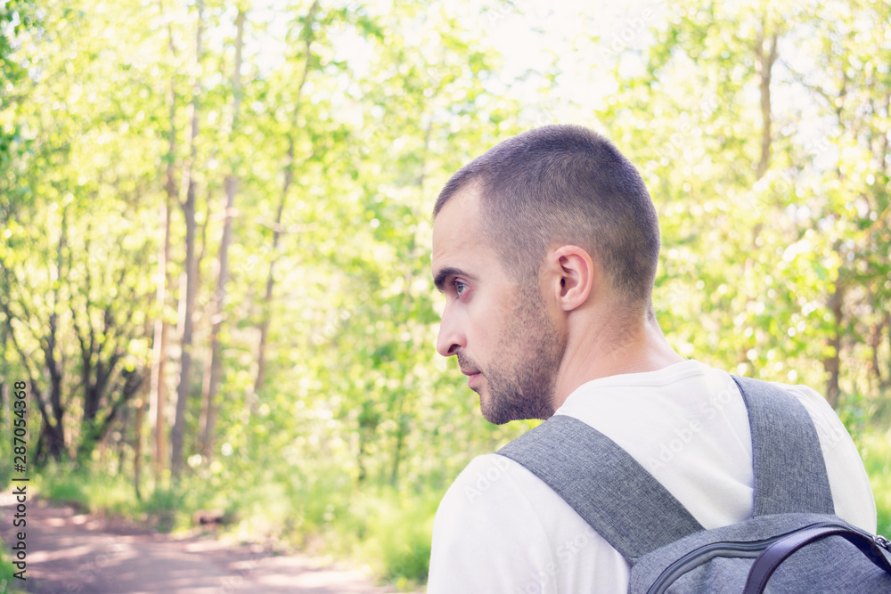 Man traveler with a backpack goes on the forest roadd, rear view, close-up, toned Man traveler with a backpack goes on the forest roadd, rear view, close-up, toned