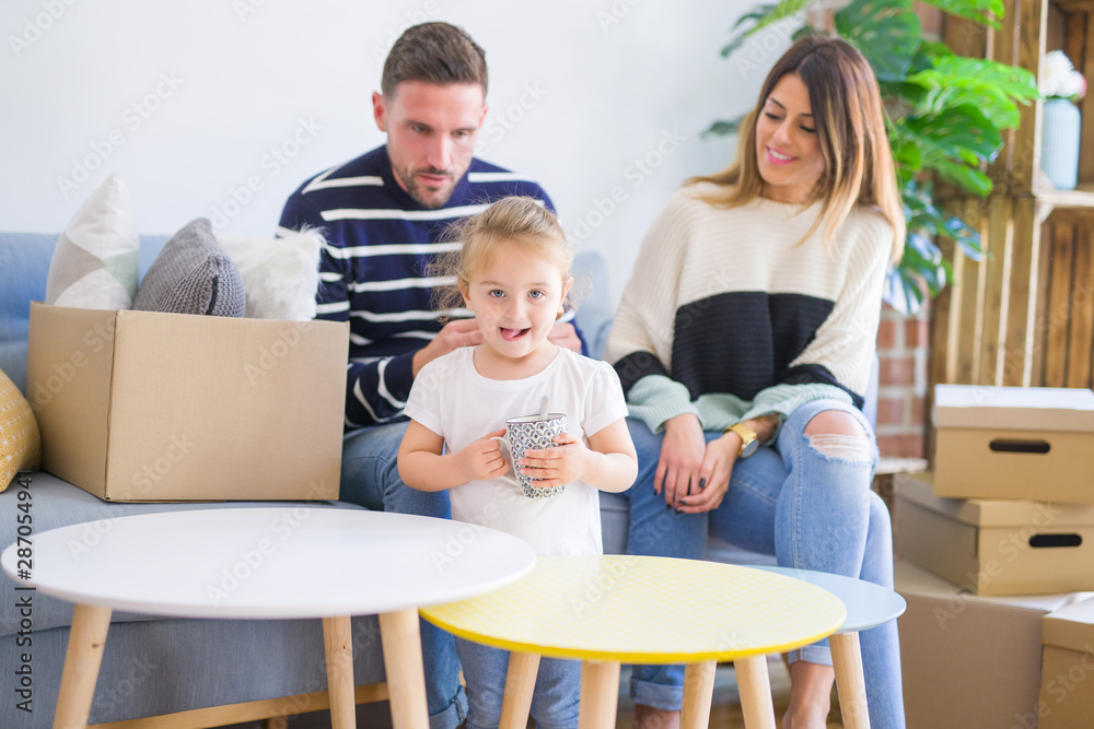 Beautiful family, parents sitting on the sofa drinking coffee looking his kid playing at new home around cardboard boxes Beautiful family, parents sitting on the sofa drinking coffee looking his kid playing at new home around cardboard boxes