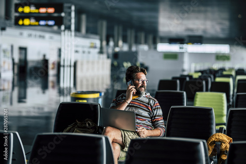 Lonely man sit down and use technology device like laptop and mobile phone at the airport gate waiting for his filght - concept of flights deleted and wait people - rights travel © simona