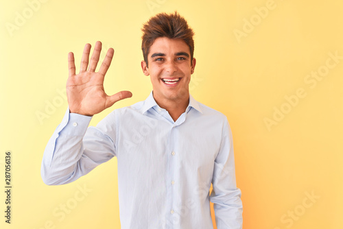 Young handsome businessman wearing elegant shirt over isolated yellow background showing and pointing up with fingers number five while smiling confident and happy.