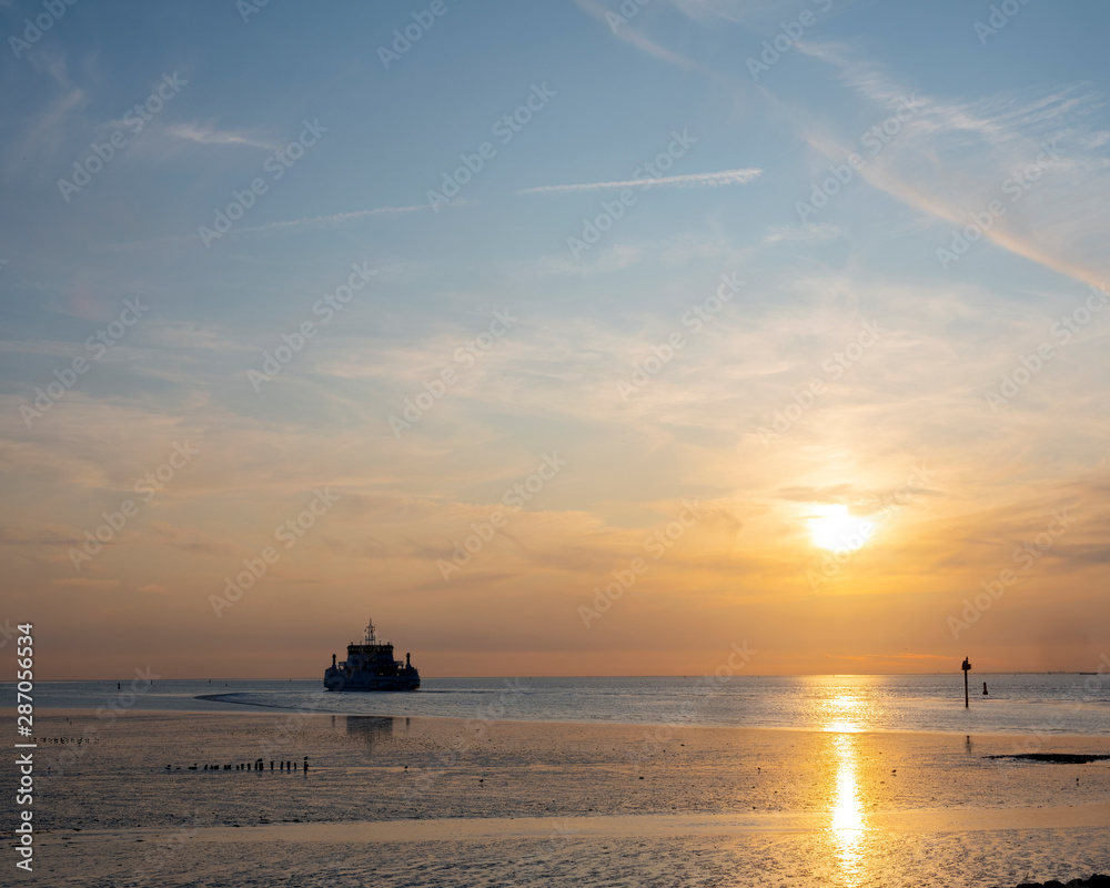 ferry from ameland arrives during sunset at harbor of Holwerd in dutch province of friesland