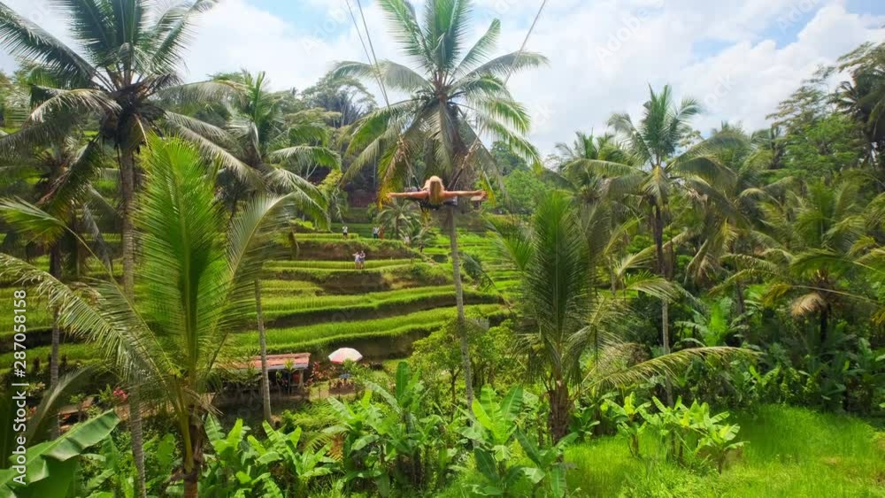 slow motion dolly shot of a young blond woman swinging over rice fields in Bali slow motion dolly shot of a young blond woman swinging over rice fields in Bali