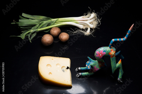 Gato de artesanía mexicana comiendose un queso sobre fondo negro photo