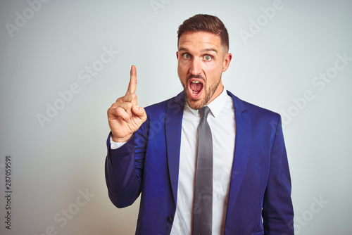 Young handsome business man over white isolated background pointing finger up with successful idea. Exited and happy. Number one.