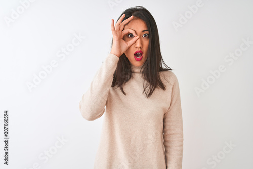 Beautiful chinese woman wearing turtleneck sweater standing over isolated white background doing ok gesture shocked with surprised face, eye looking through fingers. Unbelieving expression. © Krakenimages.com