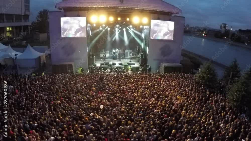 Aerial view of an open air concert in a night city - lighted stage with musicians and an enormous crowd of listeners