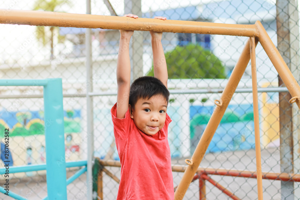 Fototapeta premium Kid exercise for health and sport concept. Happy Asian child boy playing and hanging from a steel bar at the playground. 5 years old.