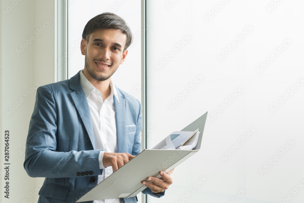 Handsome young asian businessman / manager standing folded arm on colleagues background in office / workplace. Handsome young asian businessman / manager standing folded arm on colleagues background in office / workplace.