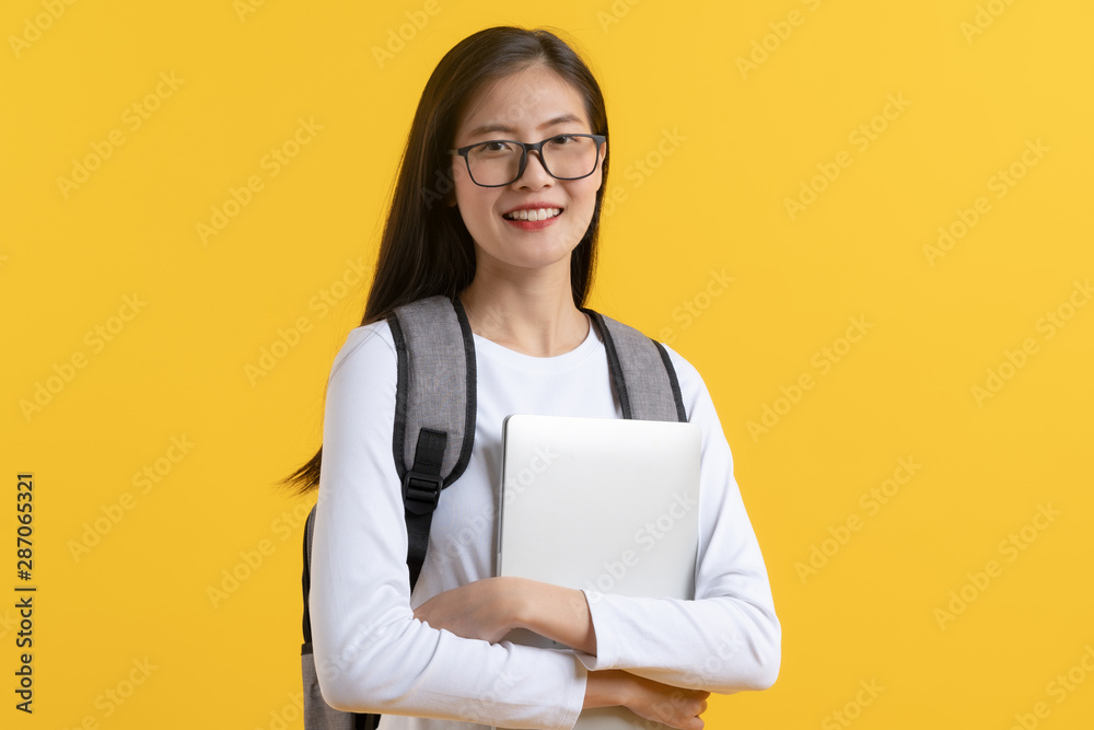 Smart asian teenager in white casual shirt nerd look carrying laptop ready to go to study isolated on yellow background in studio. Smart asian teenager in white casual shirt nerd look carrying laptop ready to go to study isolated on yellow background in studio.