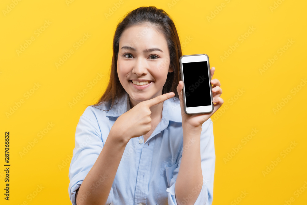 Happy beauty asian young woman showing advertise sales campaign in mobile app. Blank smartphone screen. Shot in studio isolated on yellow background. Happy beauty asian young woman showing advertise sales campaign in mobile app. Blank smartphone screen. Shot in studio isolated on yellow background.