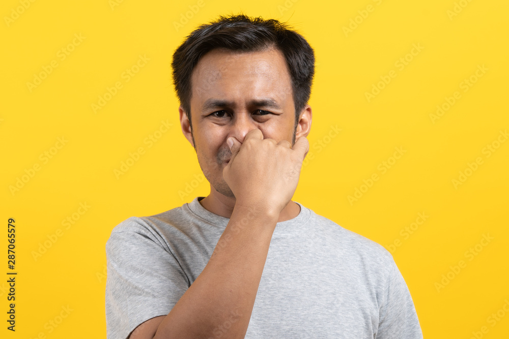 Face expression of human. Asian male smelling disgusted odor and pinching his nose in studio shoot yellow background. Face expression of human. Asian male smelling disgusted odor and pinching his nose in studio shoot yellow background.