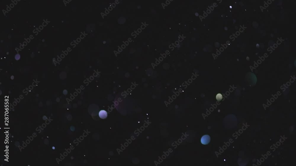 Abstract glittering particles floating bokeh. Colorful blurred dust sparkles on black background. Holiday backdrop. Slow motion 4K UHD video footage. 3840X2160
