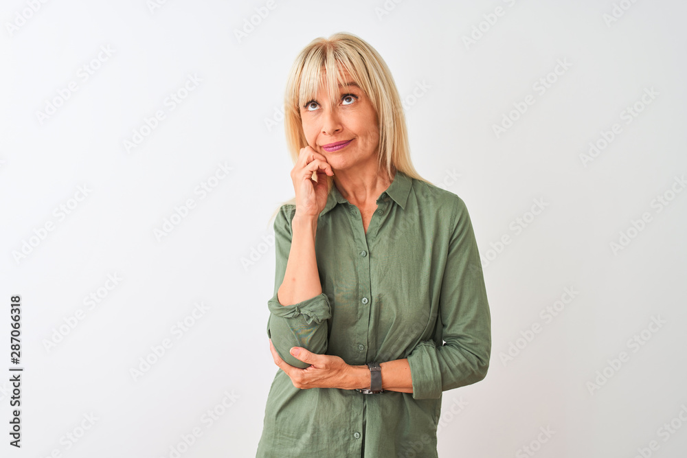 Middle age woman wearing green casual shirt standing over isolated white background with hand on chin thinking about question, pensive expression. Smiling with thoughtful face. Doubt concept. Middle age woman wearing green casual shirt standing over isolated white background with hand on chin thinking about question, pensive expression. Smiling with thoughtful face. Doubt concept.