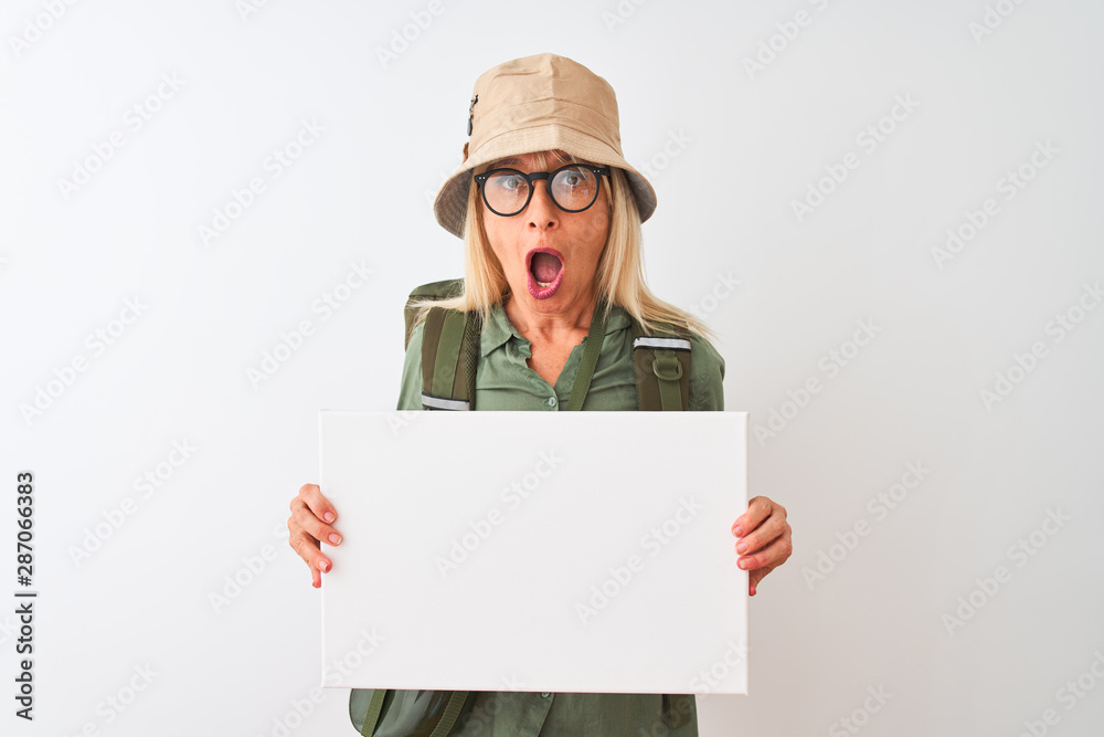 Senior hiker woman wearing canteen hat holding banner over isolated white background scared in shock with a surprise face, afraid and excited with fear expression Senior hiker woman wearing canteen hat holding banner over isolated white background scared in shock with a surprise face, afraid and excited with fear expression