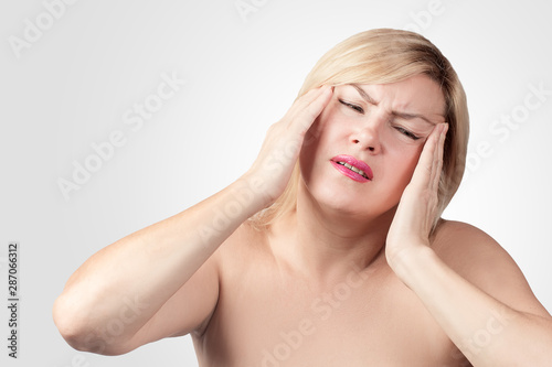 A tired upset middle-aged woman suffers from severe chronic headache, migraine, dizziness, during menopause. Concept of zhesky health.