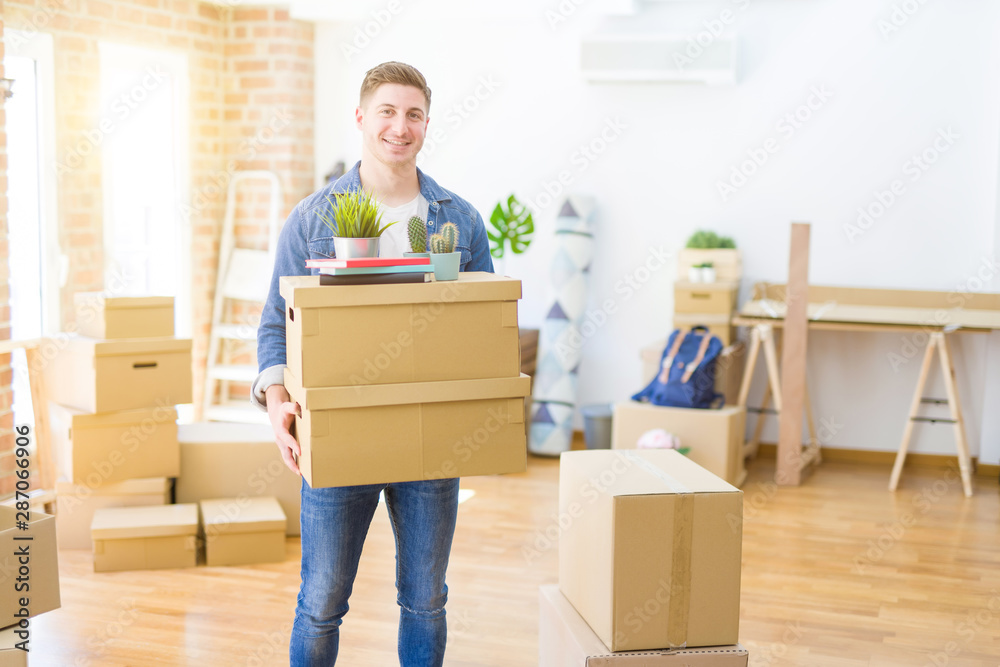 Handsome young man smiling happy moving to a new home, very excited holding cardboard boxes at new apartment Handsome young man smiling happy moving to a new home, very excited holding cardboard boxes at new apartment
